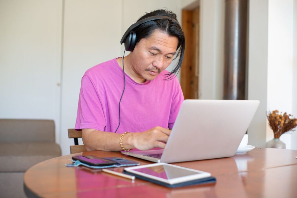 Lelaki dalam panggilan video memakai headphone di laptop di rumah