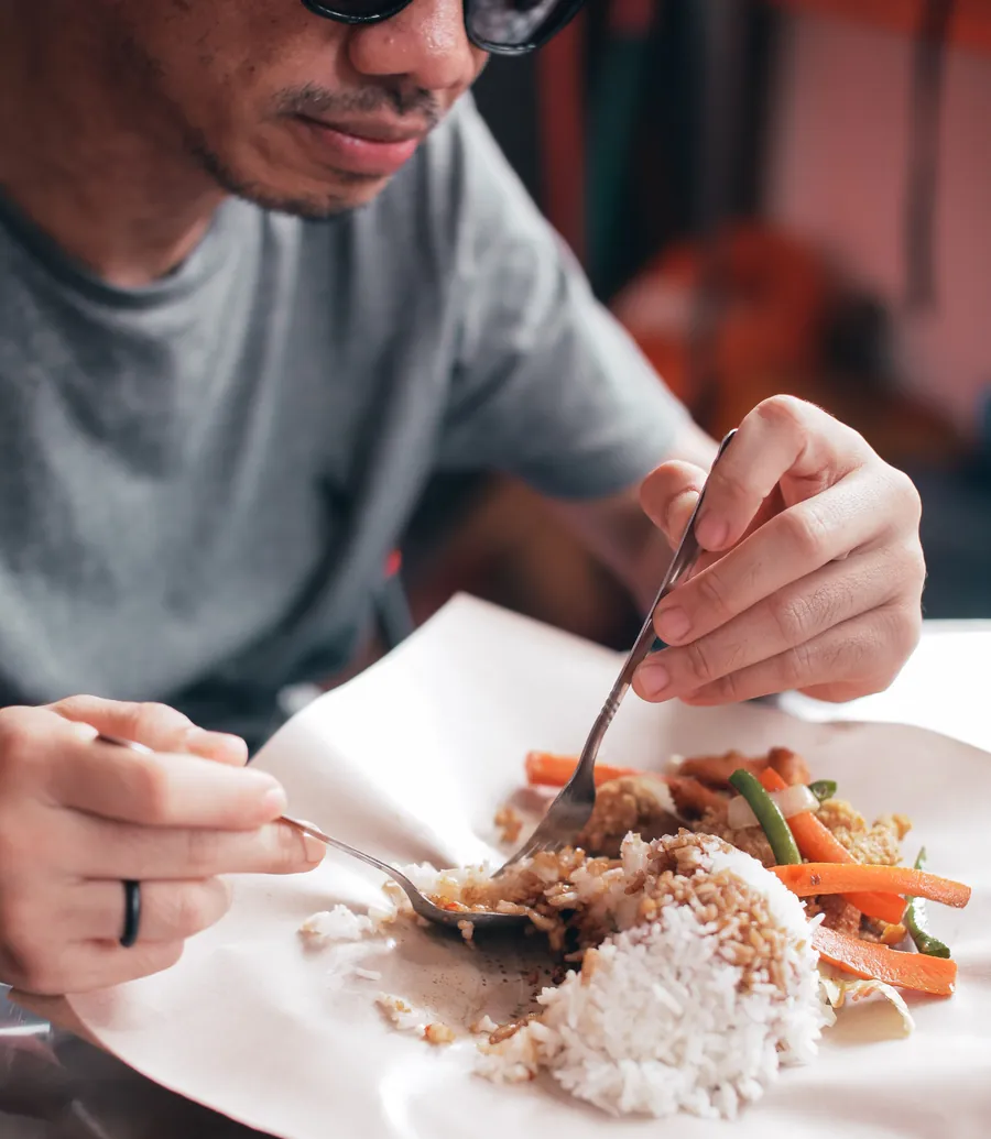 Seorang lelaki menikmati nasi campur dengan sayur dan telur di gerai makan tempatan
